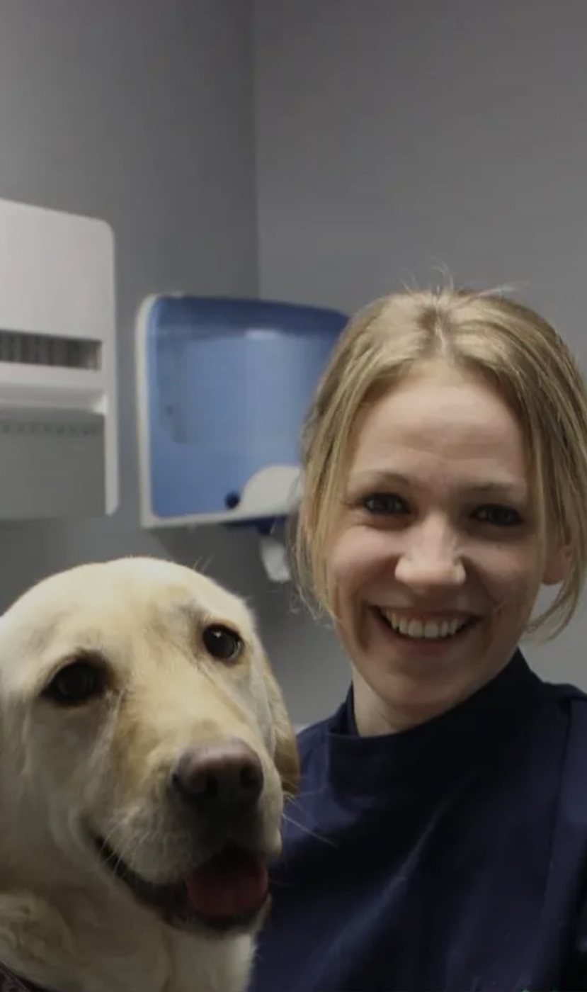 Sonia smiling beside a golden Labrador